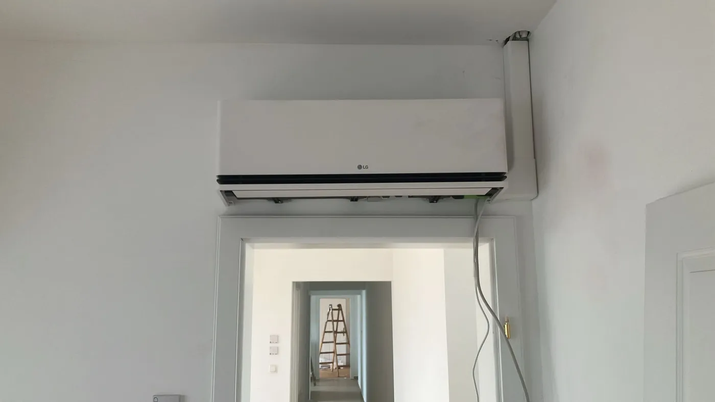 LG Wandgerät über einer Altbau-Tür, die Leitung läuft im Kanal in der Raumecke zur Decke