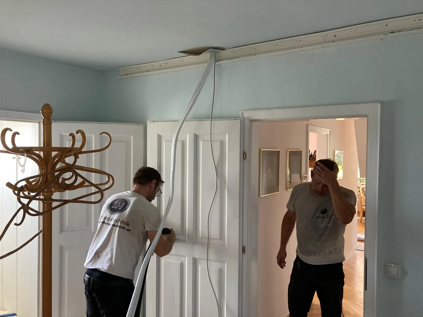 Zwei Monteure von IH Lüftungstechnik ziehen Kältemittelleitungen durch die Decke einer Altbauwohnung